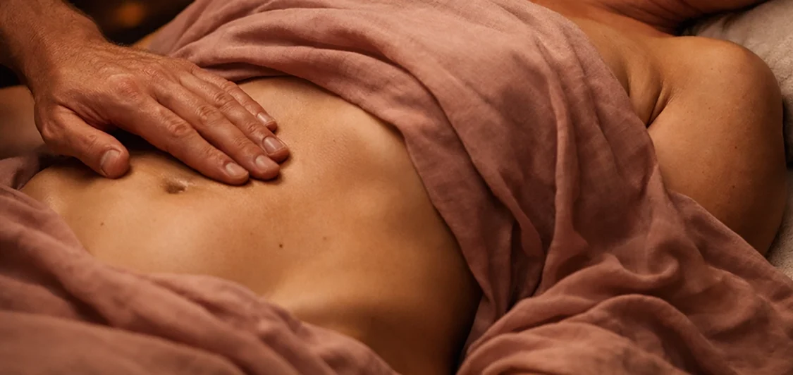 Eine Hand berührt sanft einen Bauch in sanften, warmen Farben, bei Beckenbodenmassage.