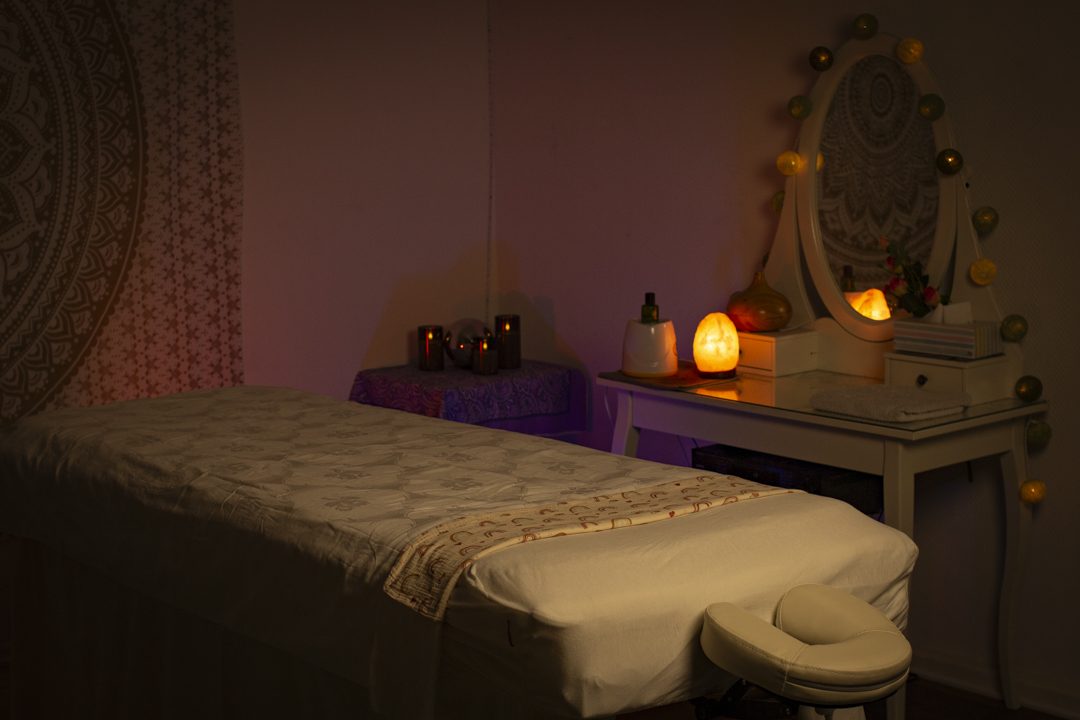 Achtsame Frauenmassage Hannover – Wohlfühlatmosphäre & tiefe Entspannung | hannovermassage.de Entspannendes Massagezimmer in warmem Purpurlicht in Hannover mit Mandala-Wandteppich, Massageliege, Salzlampe, Kerzen und duftenden Ölen