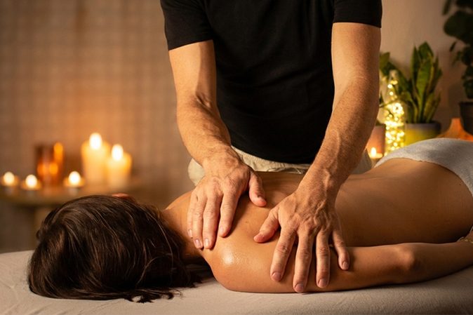 Eine Person erhält eine Rückenmassage in einer entspannenden Umgebung mit Kerzen.