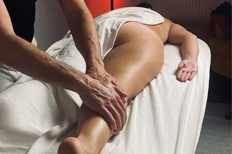 Eine Person erhält eine Massage am Bein, während sie auf einer Liege liegt.